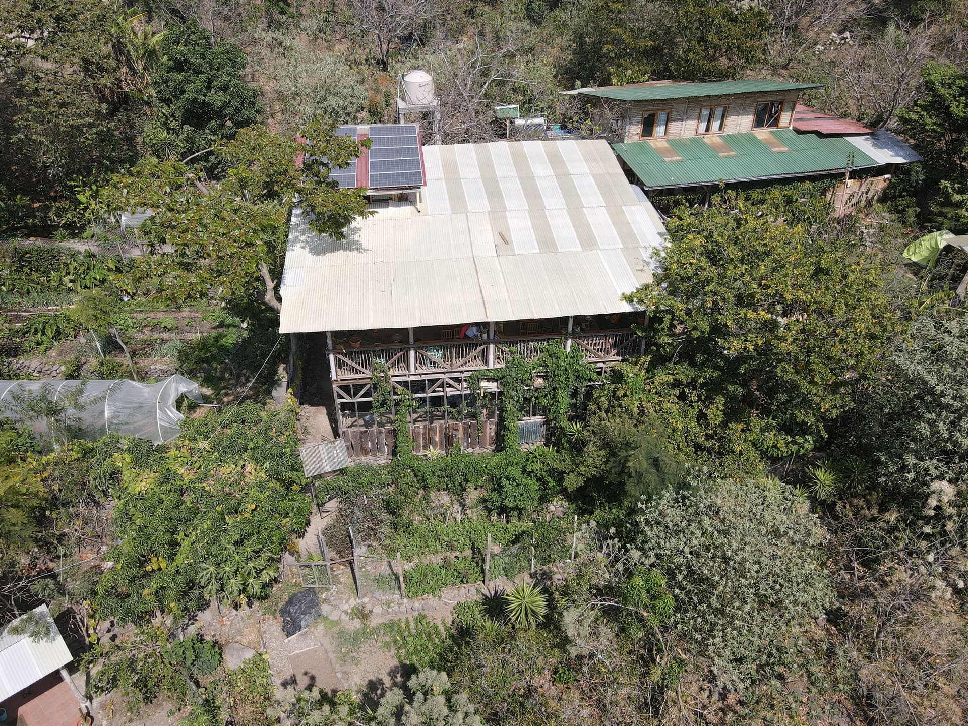 Aerial view of the main building at Granja Tz’ikin, solar panels and the water tank on the roofline, growing beds stepping down the slope