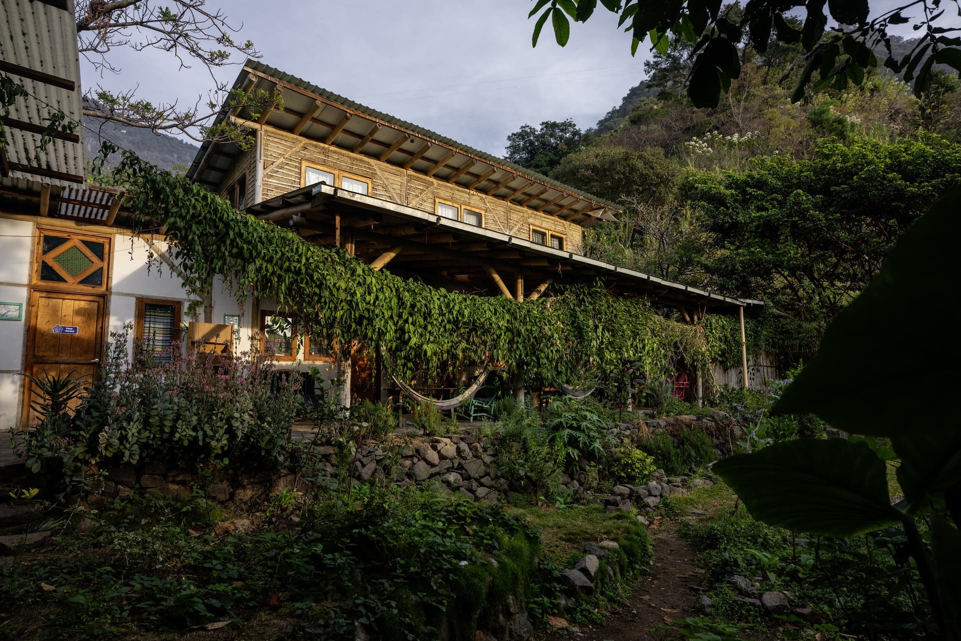 The guest house at Granja Tz’ikin in evening light — hammocks under the vine-covered veranda, stone terraces below