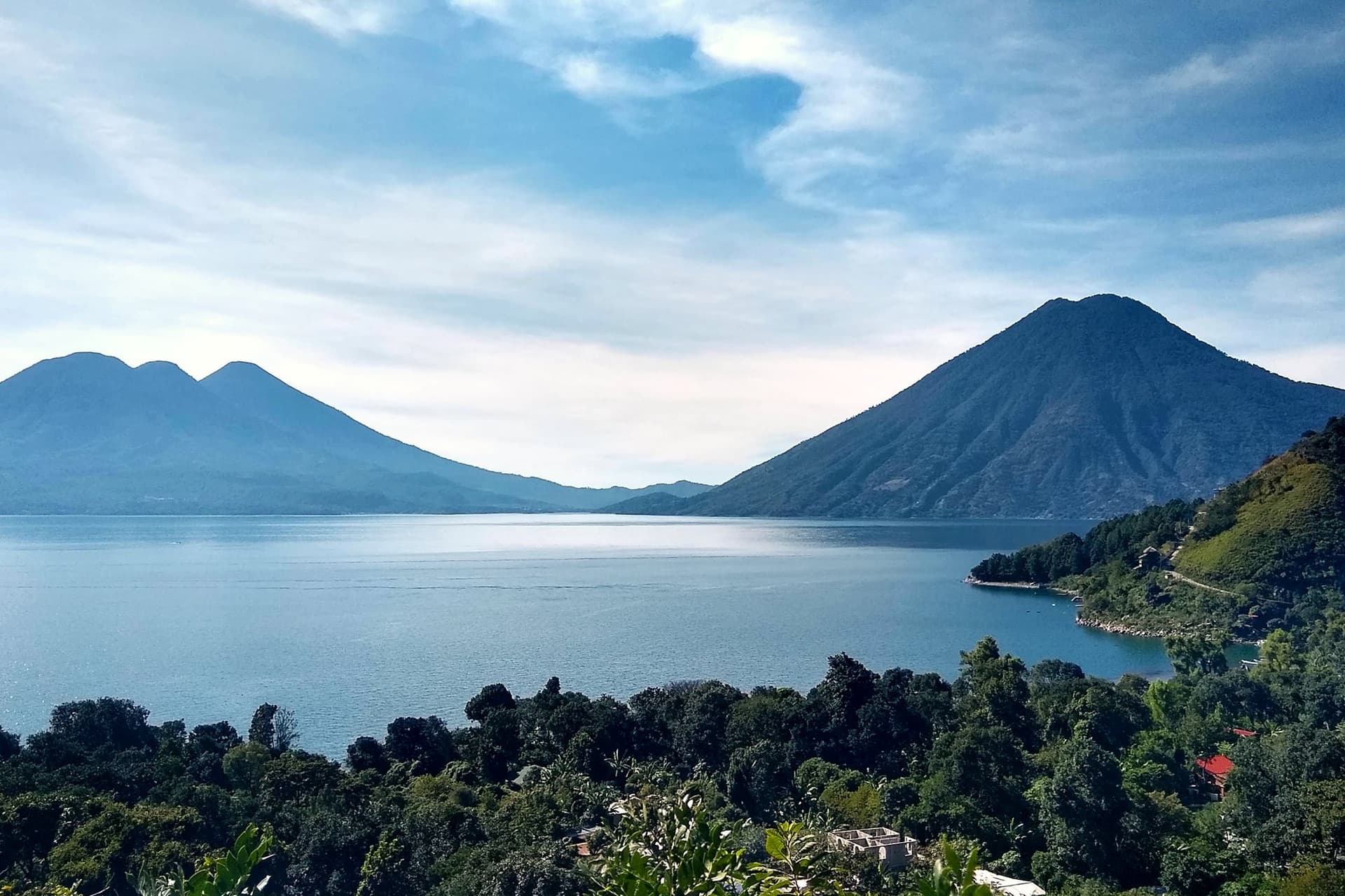 Lake Atitlán in flat calm with two volcanoes rising beyond the far shore