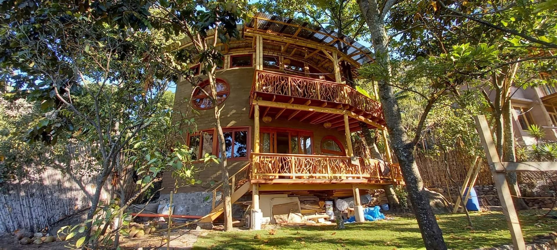 Casa Girasol seen from the garden — a two-level adobe and timber home with wrap-around balconies, built around a standing tree