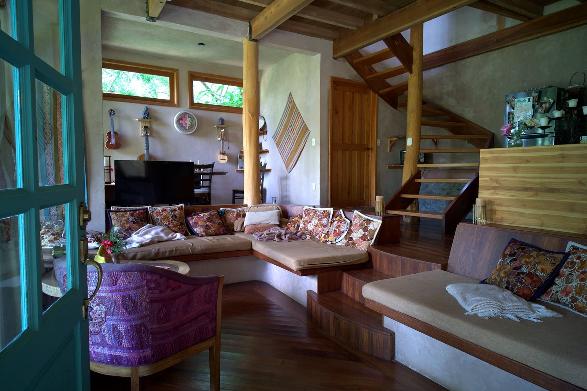 Inside Casa de Surya — earth-plastered walls, a round timber post, built-in banquette seating and an open hardwood staircase