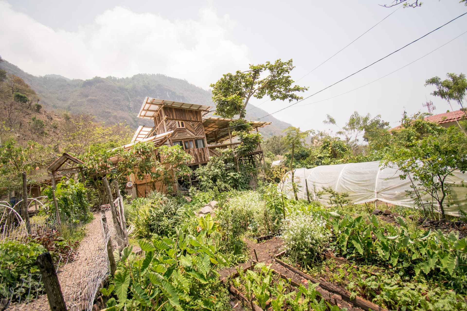 Granja Tz’ikin under the mountain — the timber tower above the growing beds, polytunnel and planted paths of the farm