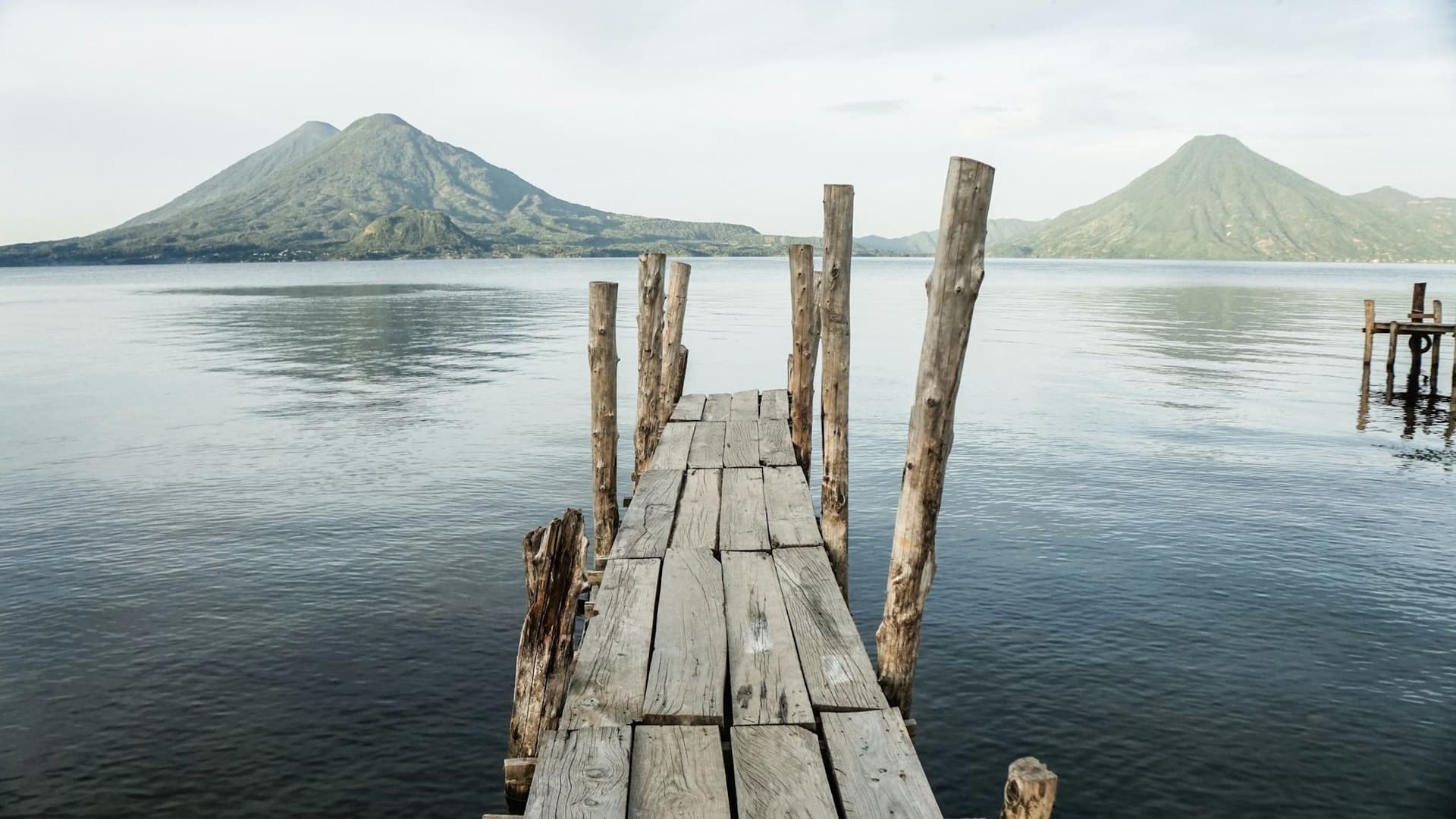 A wooden dock reaching into Lake Atitlán, ringed by volcanoes