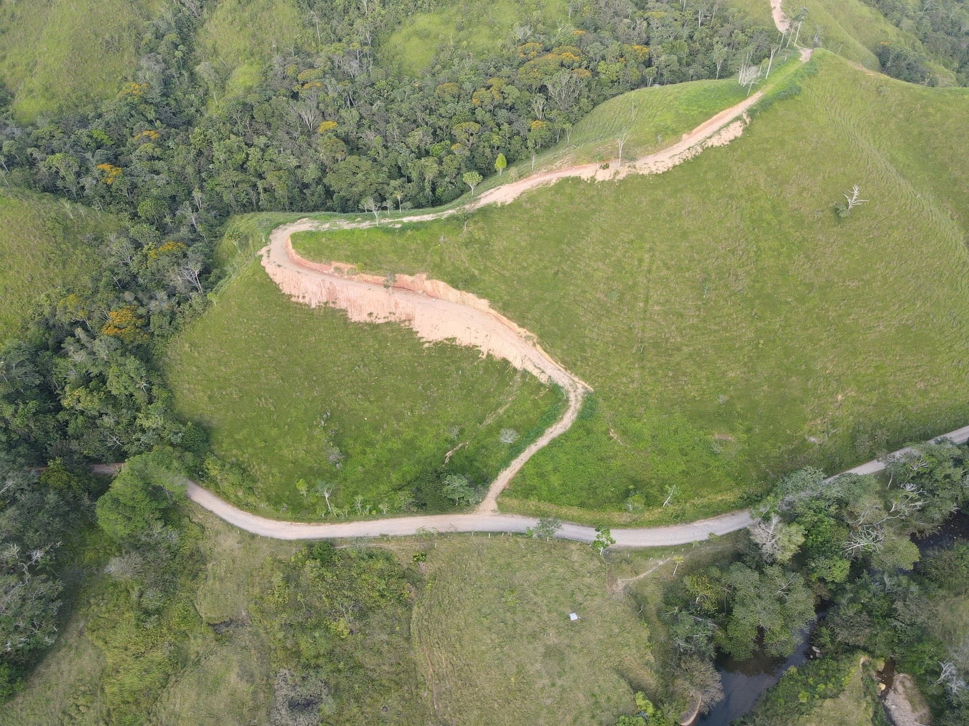 Vista aérea de una finca: potreros en la ladera, el camino cruzando y la quebrada arbolada abajo