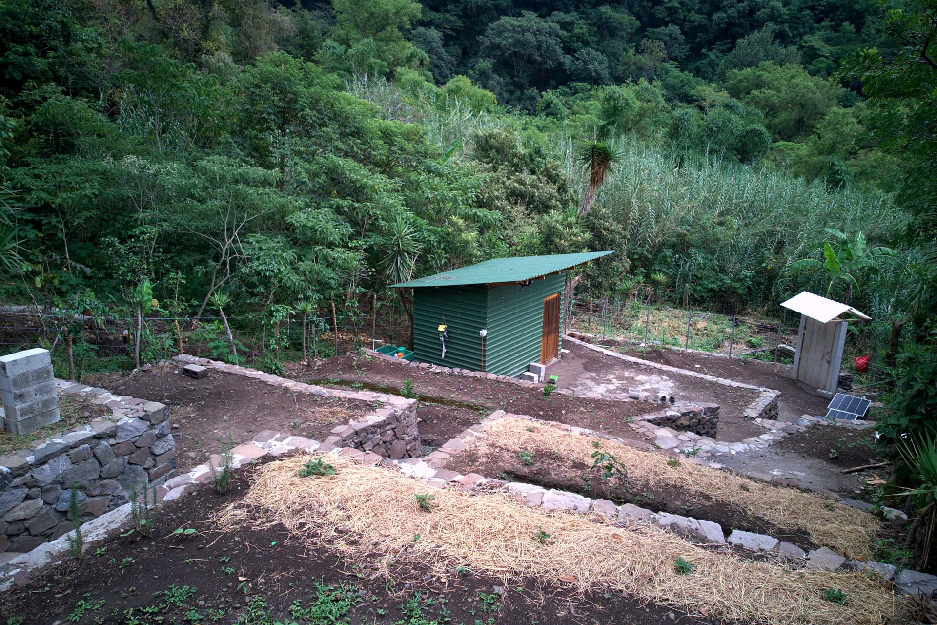 Dry-stone terrace beds under construction at Granja Tz’ikin, with a workshop shed and raised beds